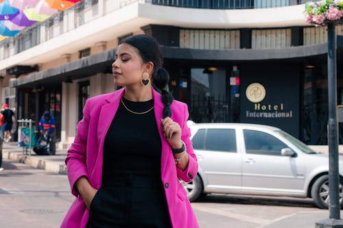 A woman in a pink blazer and black pants walking down the street