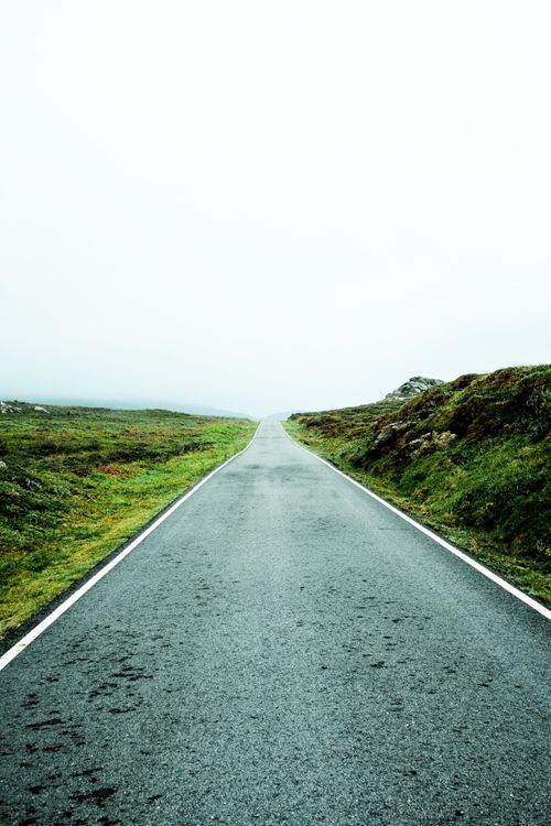 Free An empty rural road fades into the fog, flanked by lush greenery and misty hills. Stock Photo