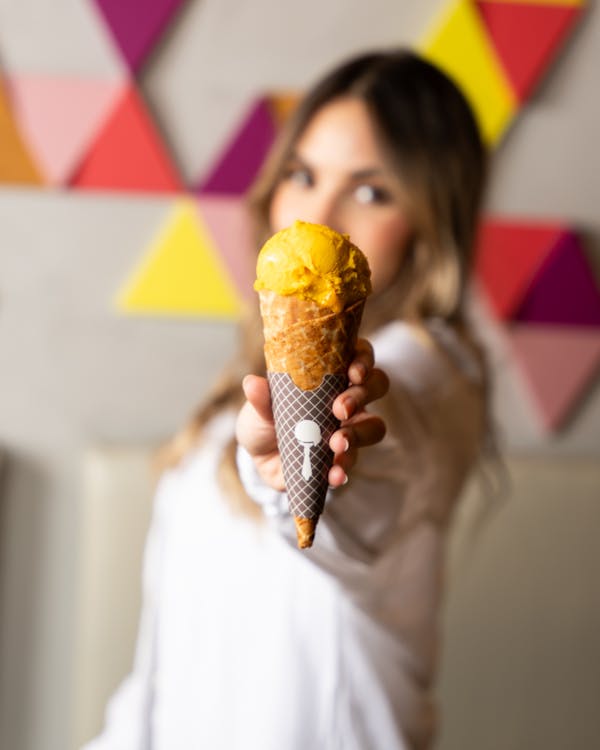 A woman holding up an ice cream cone with a yellow and orange swirl