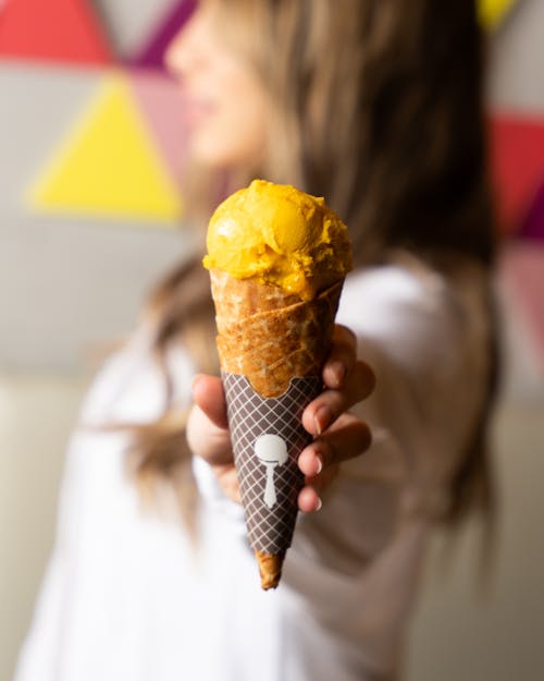A woman holding up an ice cream cone with a yellow topping