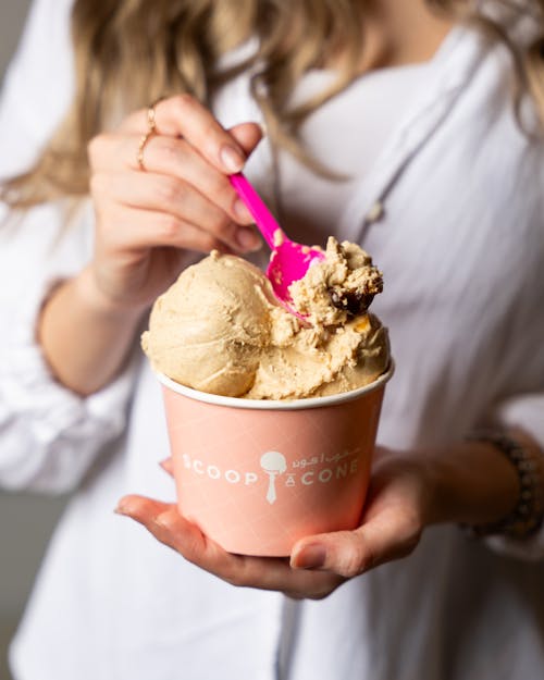 A woman holding a pink spoon in her hand holding a scoop of ice cream