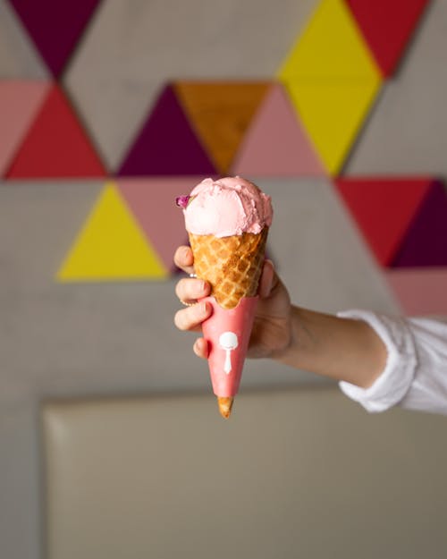 A person holding an ice cream cone in front of a wall