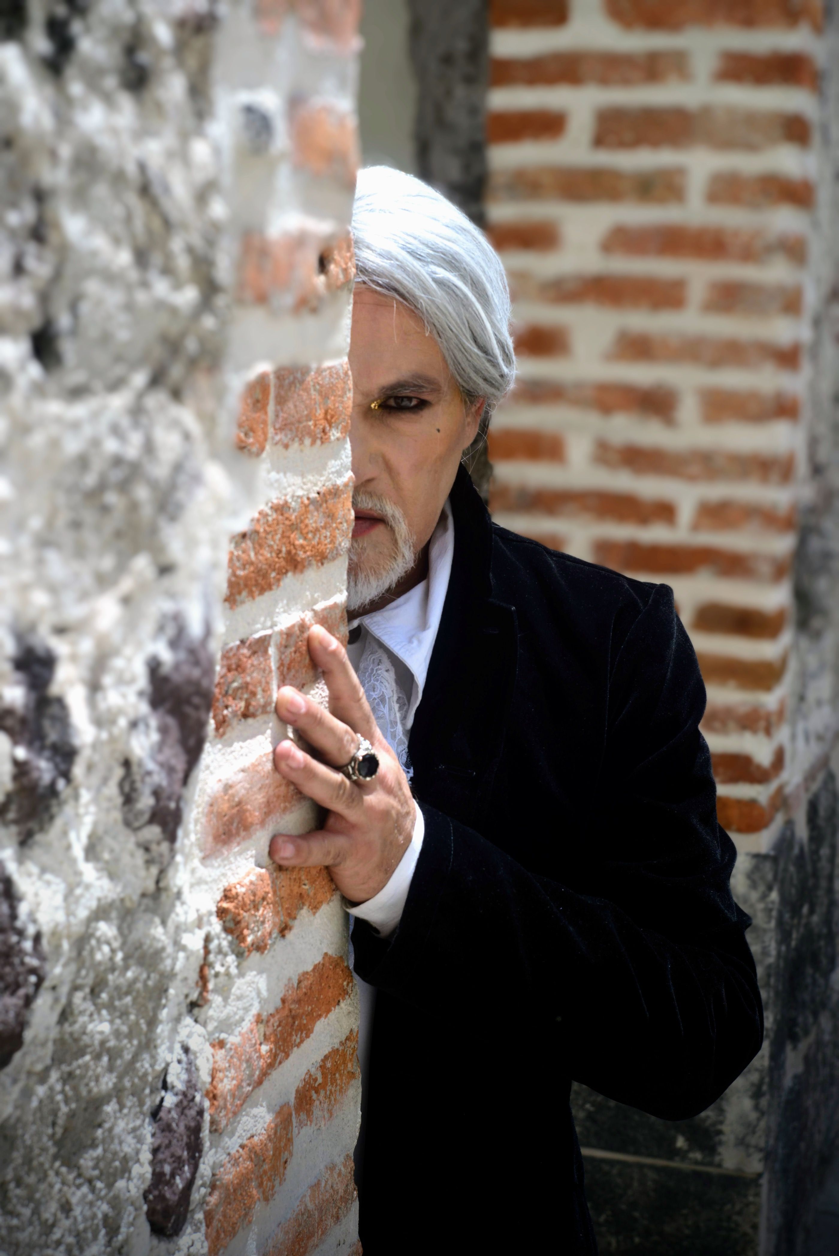 Elderly man with grey hair in a suit partially hidden behind a brick wall in Mexico City.