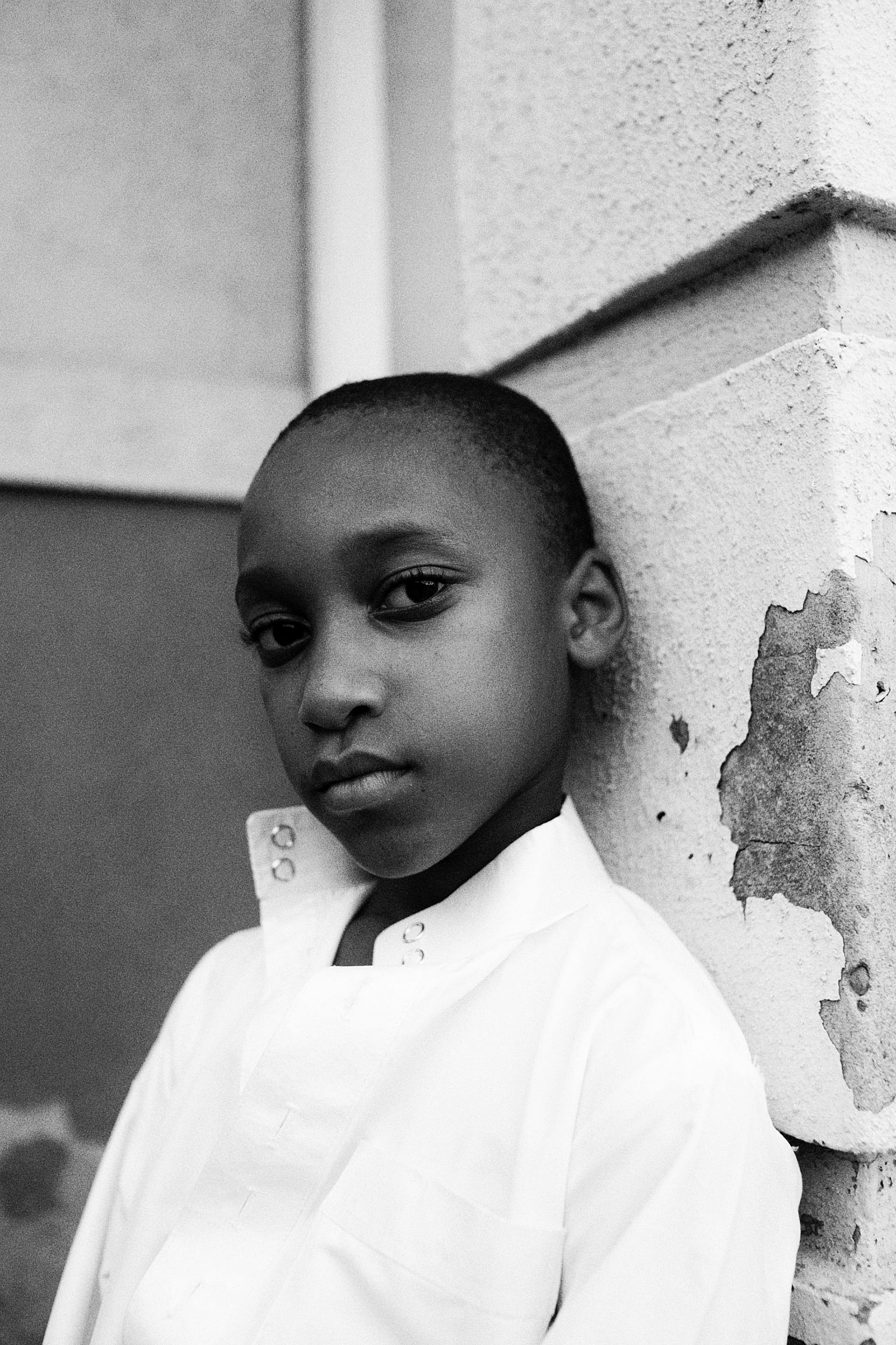 Thoughtful black and white portrait of a young boy leaning against a wall.