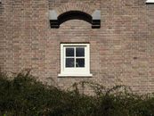 Close-up of a traditional brick wall with a small window in Amsterdam, Netherlands.