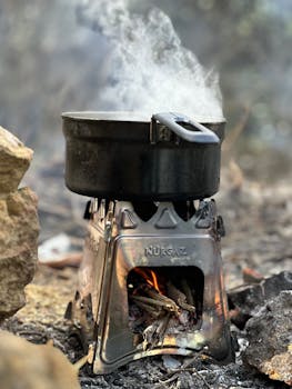 Black pot boiling over a portable wood-burning stove outdoors.