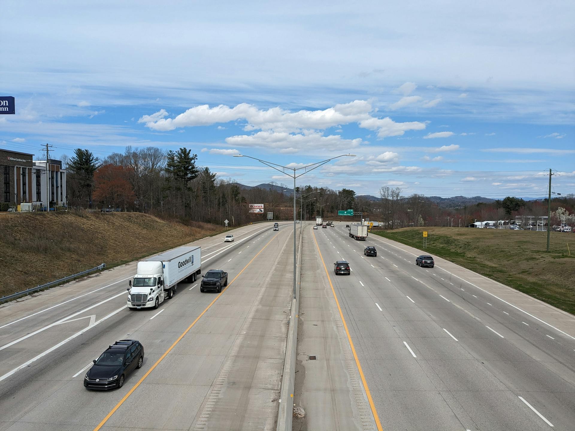 A clear aerial view of a wide urban highway with cars and trucks moving under a blue sky.