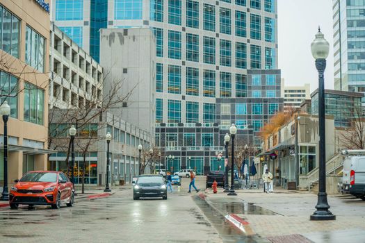 City street view featuring pedestrians and modern high-rise buildings on a rainy day.