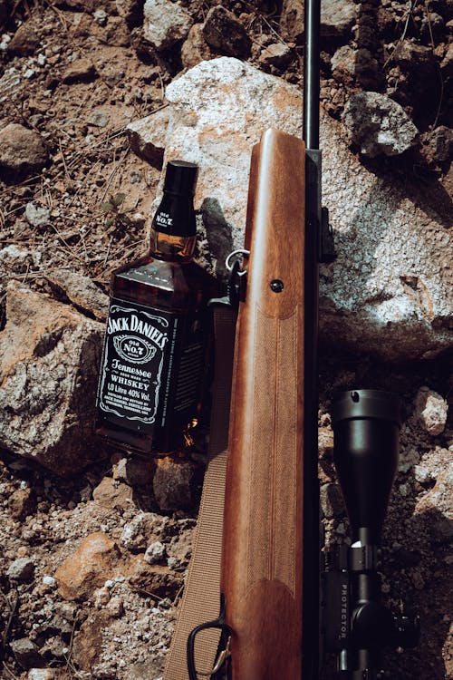 A rifle and bottle of jack daniels on the ground