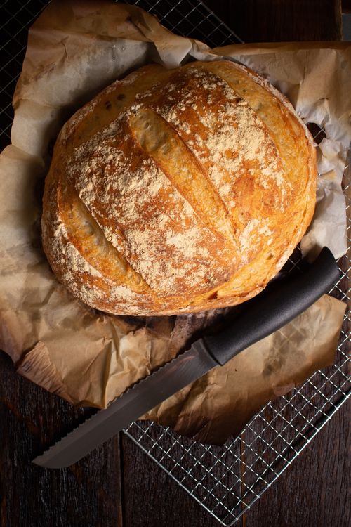 Free Top view of rustic artisan bread on parchment paper with serrated knife on a wooden table. Stock Photo