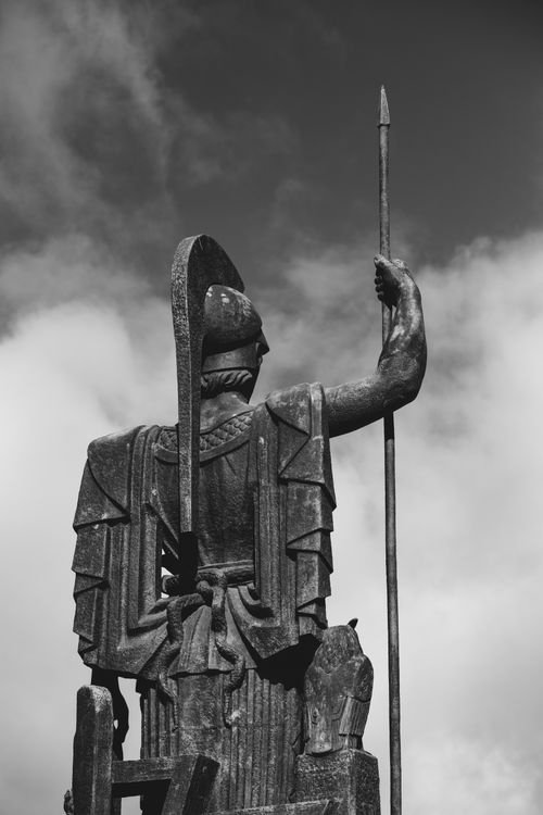 Free Dramatic black and white photo of a warrior statue in Madrid with a spear against a cloudy sky. Stock Photo
