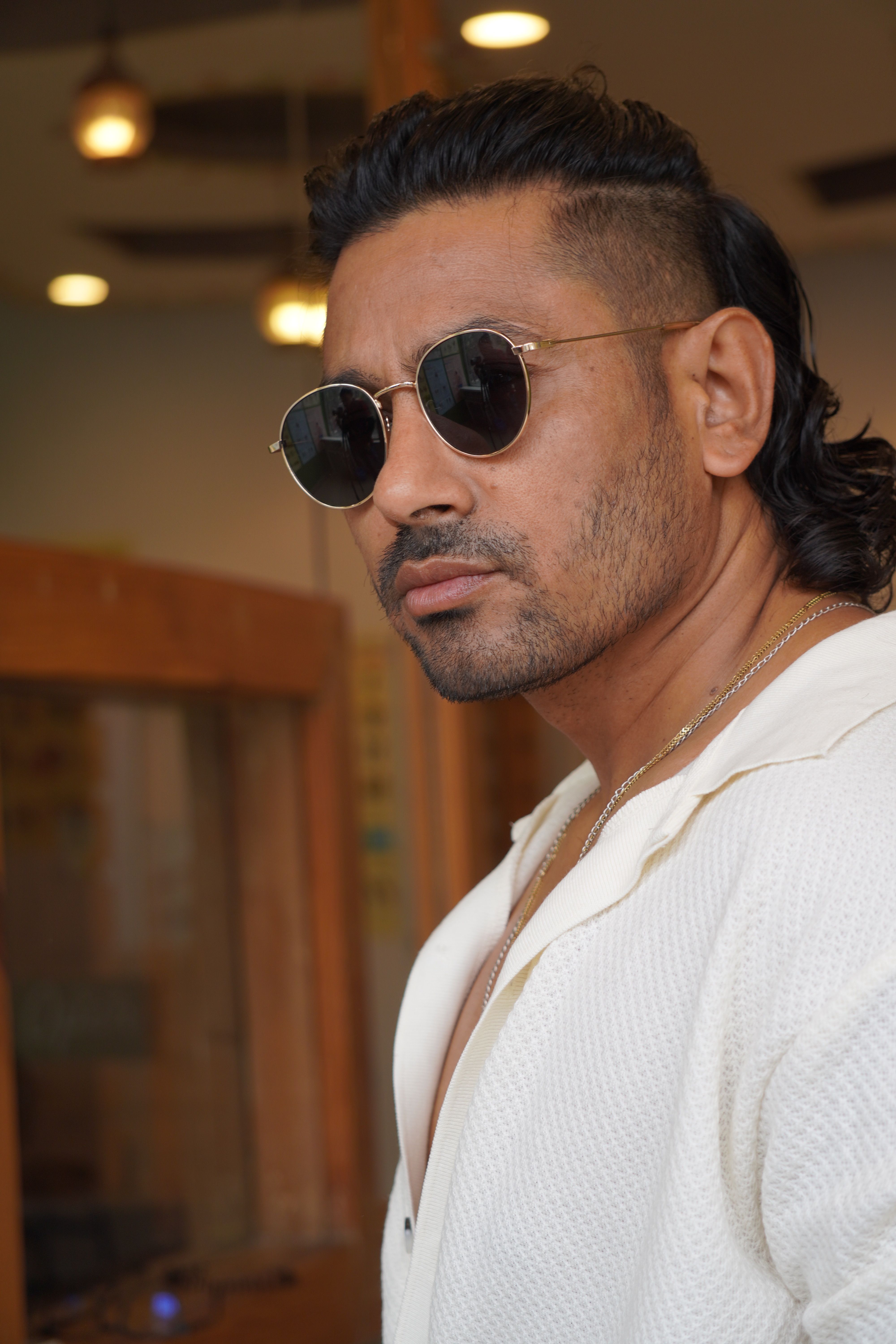 Confident man posing indoors with sunglasses, exuding modern style and fashion.