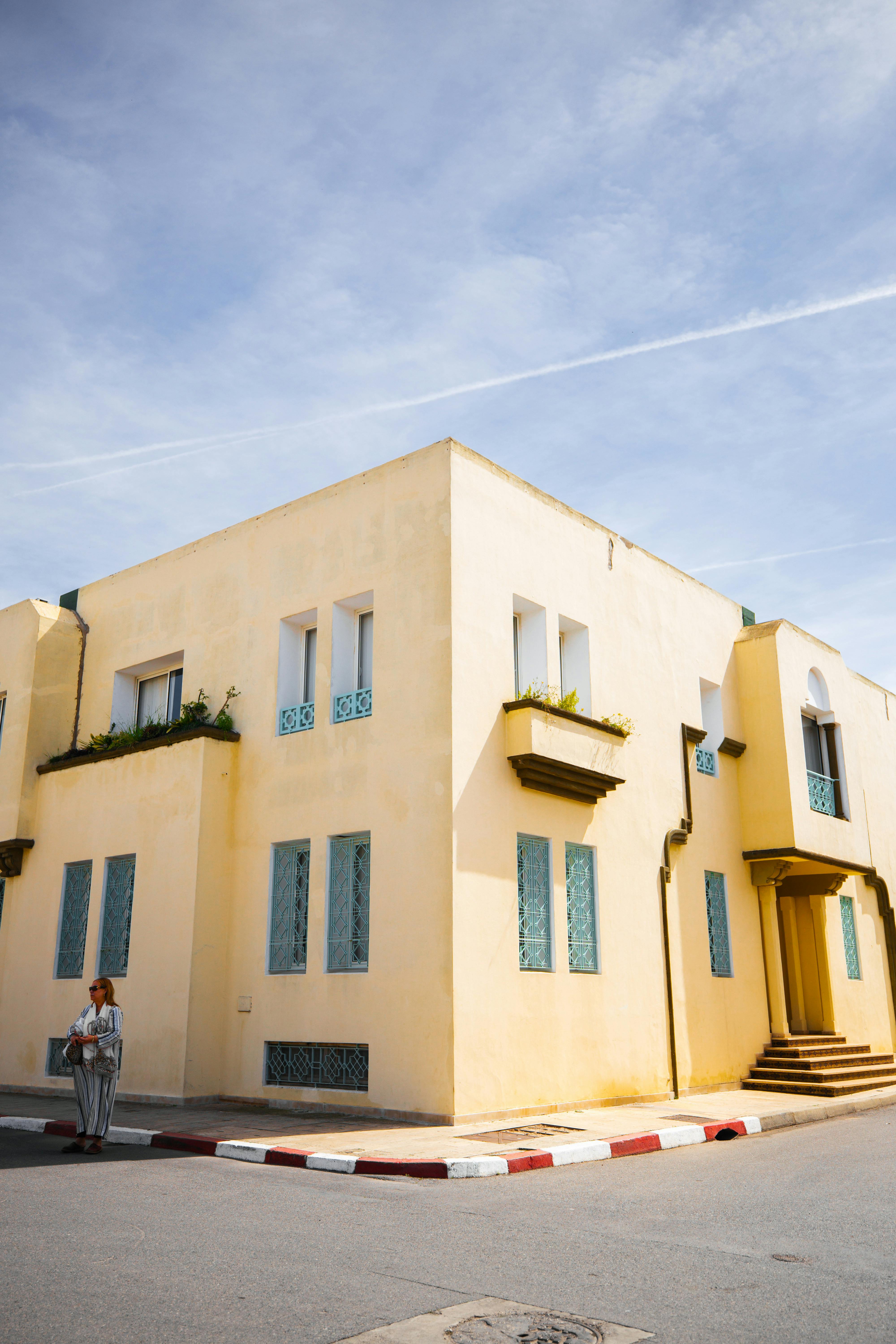 Free A stylish yellow building in a sunny urban setting with a lone adult standing on the corner. Stock Photo