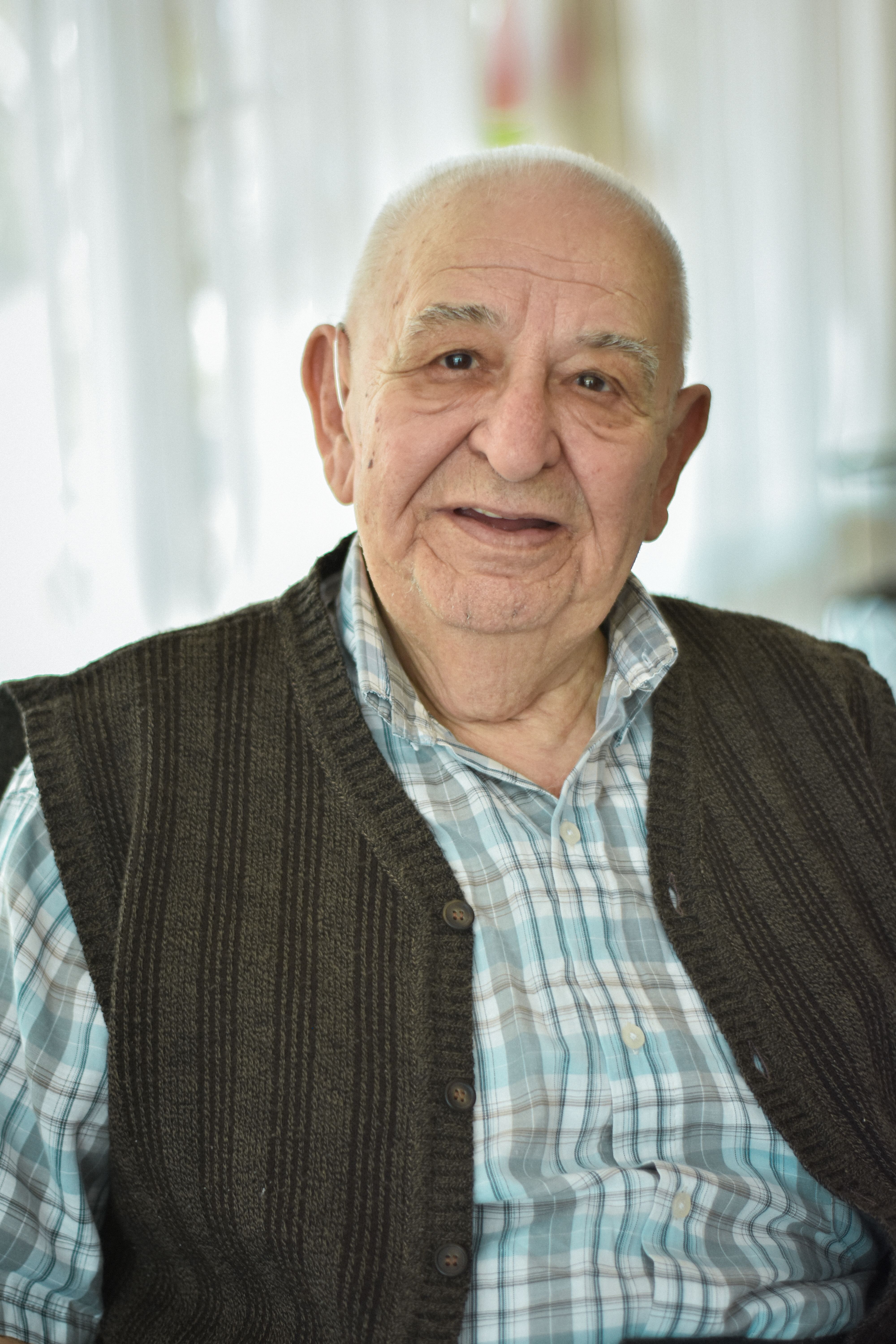 Friendly elderly man in vest and shirt, smiling indoors.