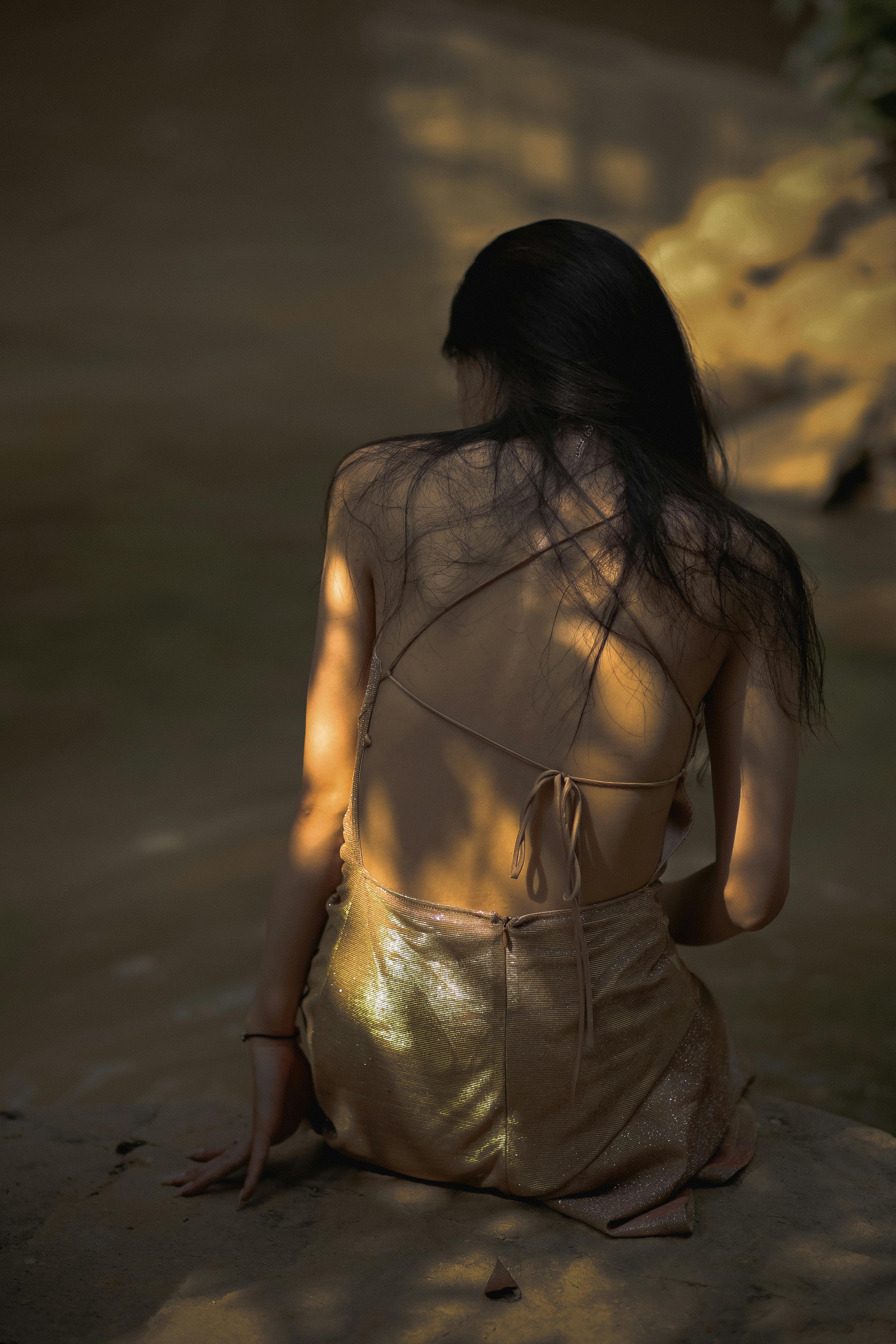 A woman in a stylish dress sits on the beach, showcasing elegant fashion photography with captivating shadows.