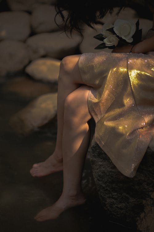 Woman Wearing Golden Dress Sitting Among Rocks