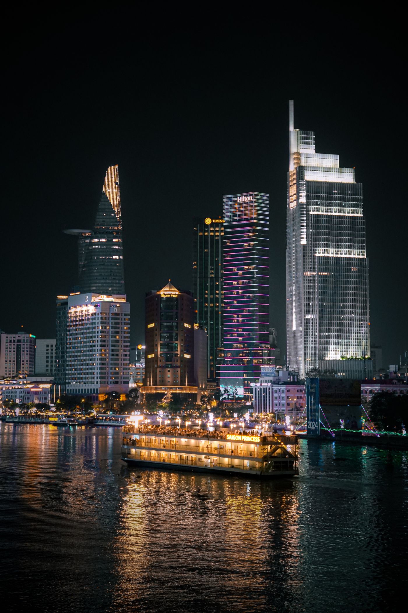 Saigon River at night with the Bitexco tower and a lit dinner cruise boat passing
