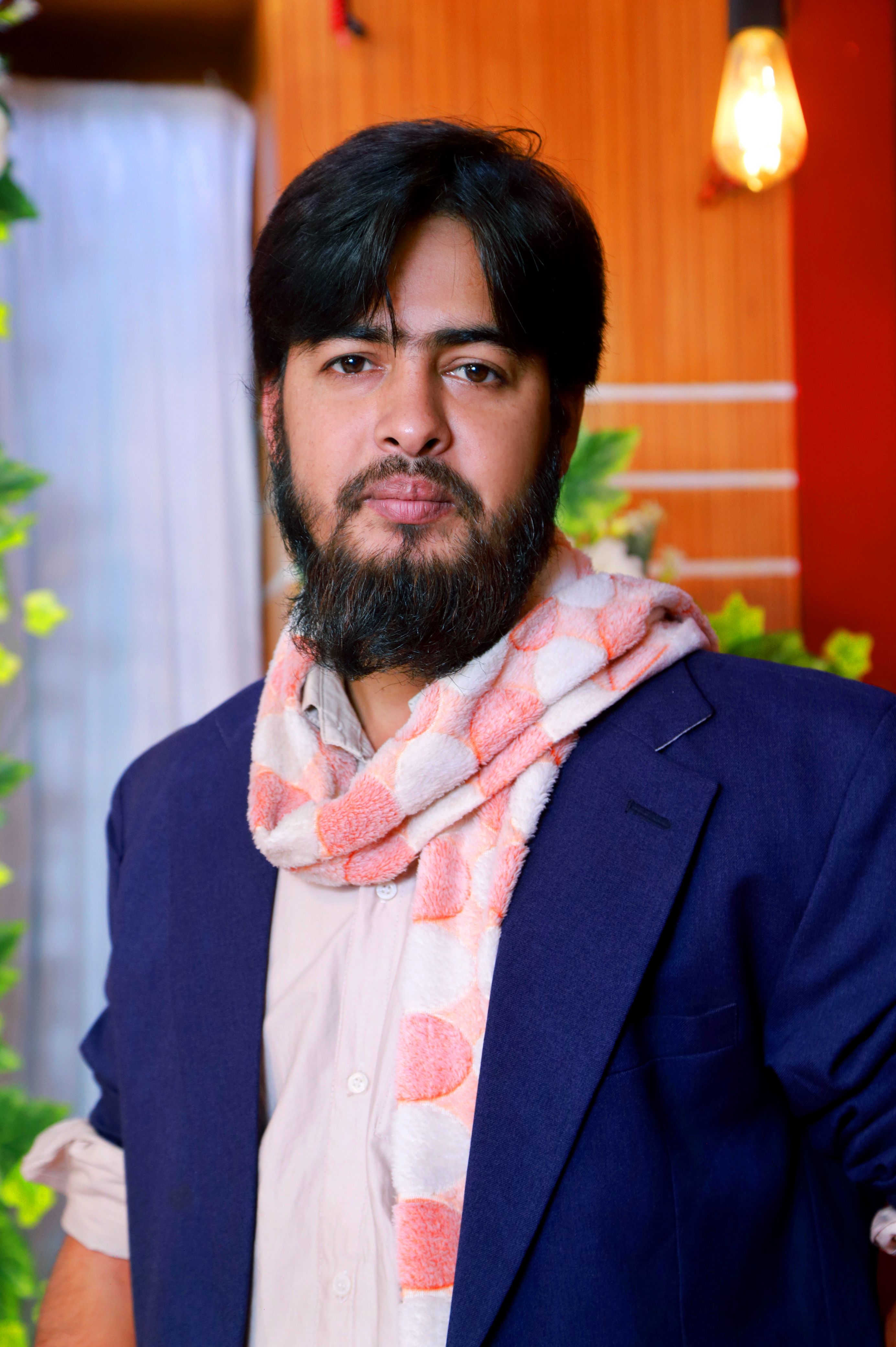 Portrait of a man in a stylish navy jacket and pink scarf indoors.