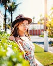 一位时尚女性戴着帽子和眼镜，身穿花卉夏装，在户外享受阳光明媚的一天