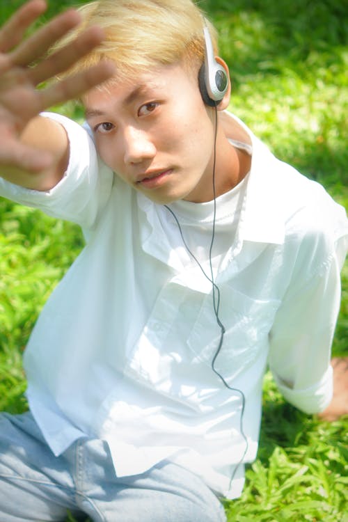 Young Man in White Shirt with Headphones Sitting on Grass