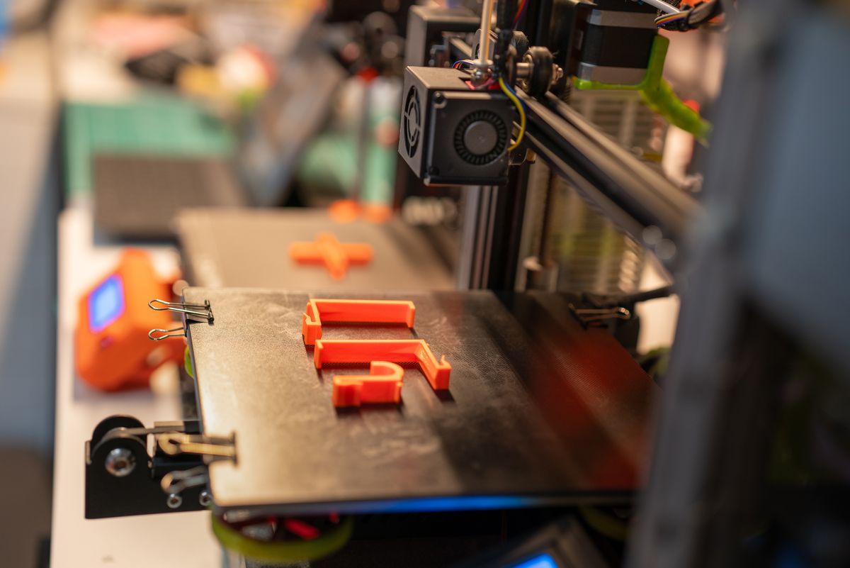 Detailed view of a 3D printer creating an orange plastic part showcasing advanced technology