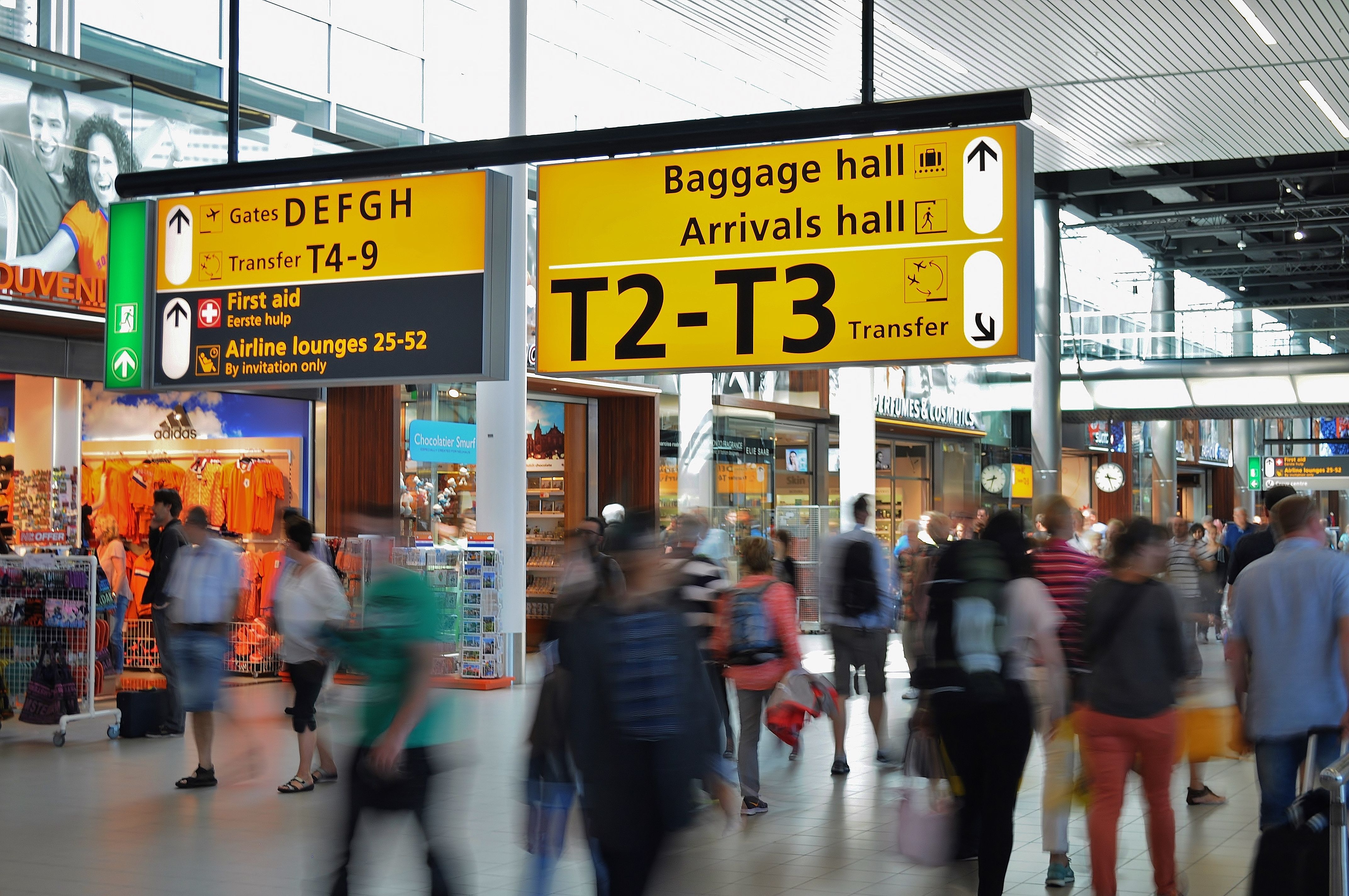 Travellers walk through an airport terminal beneath signs for arrivals, baggage hall and transfers
