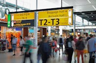 机场里人群拥挤，行李在运动模糊中移动，抵达大厅的标志清晰可见