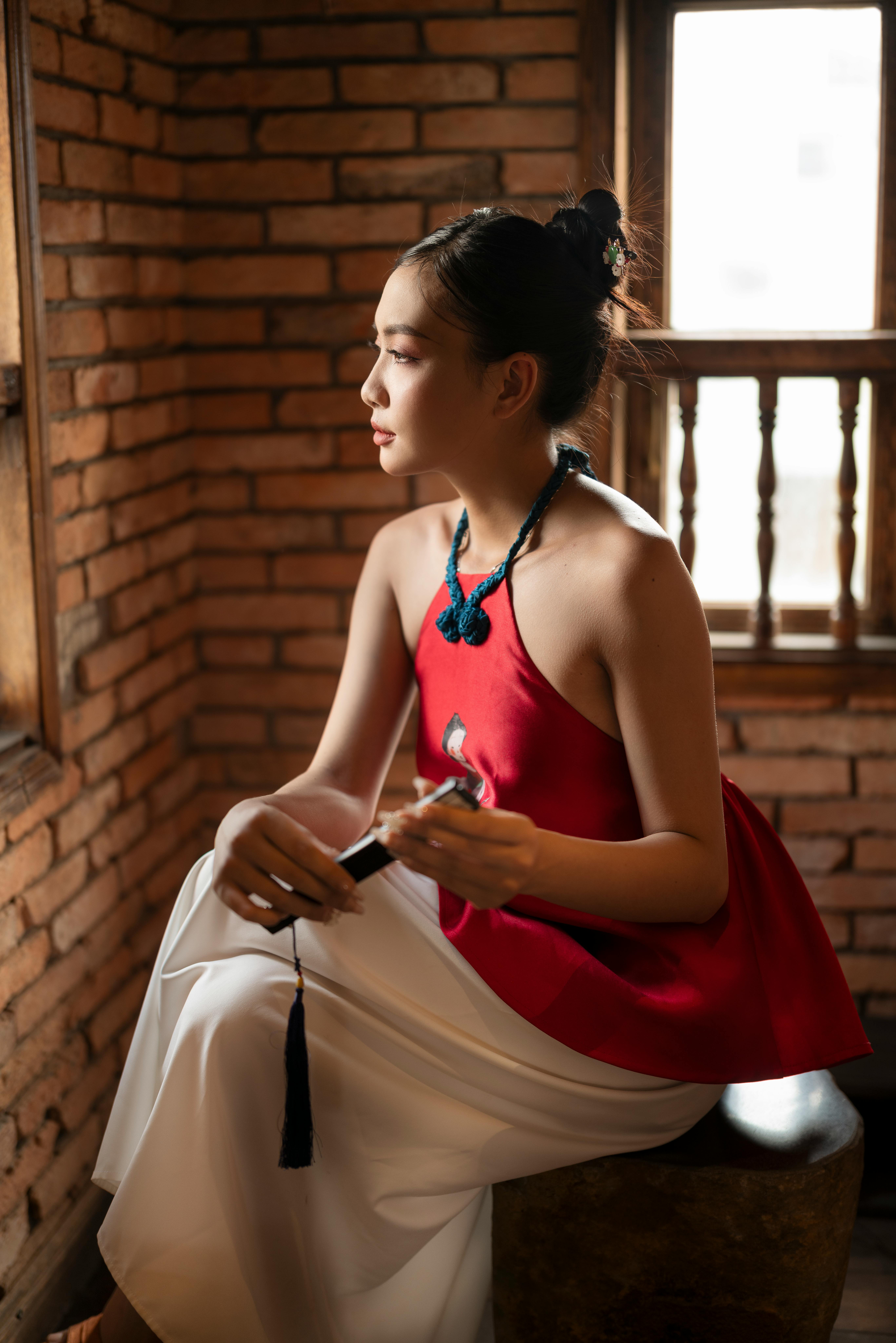 Portrait of a woman in elegant fashion, sitting indoors with brick wall background.
