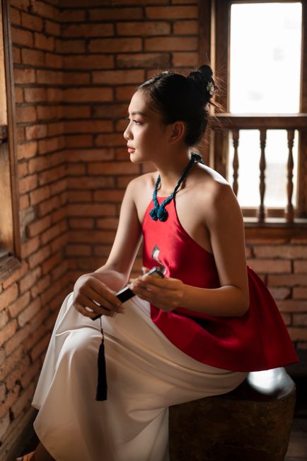 Portrait of a woman in elegant fashion, sitting indoors with brick wall background.