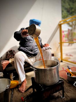 A man seated indoors pouring broth into a large pot, focusing on traditional cooking methods.