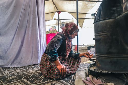 Free An elderly woman wearing a floral dress and headscarf cooks inside a rural tent. Stock Photo