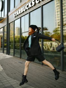 Fashionable woman jumping outside a city cafe, exuding energy and style.