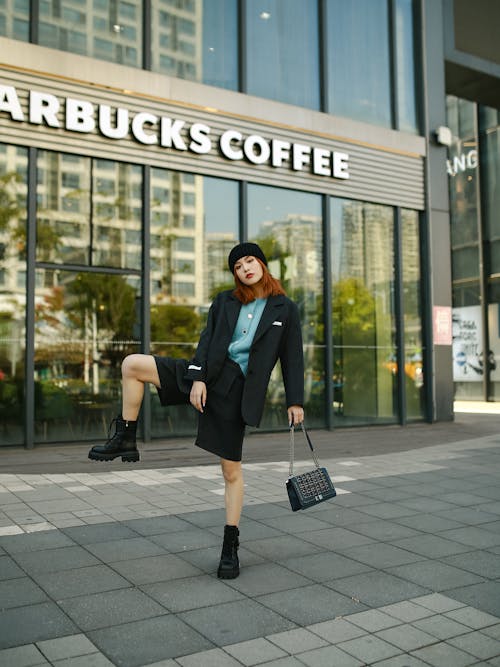 A woman in a skirt and boots is posing outside starbucks