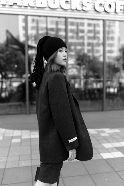 Stylish woman in winter coat and hat posing on urban sidewalk.