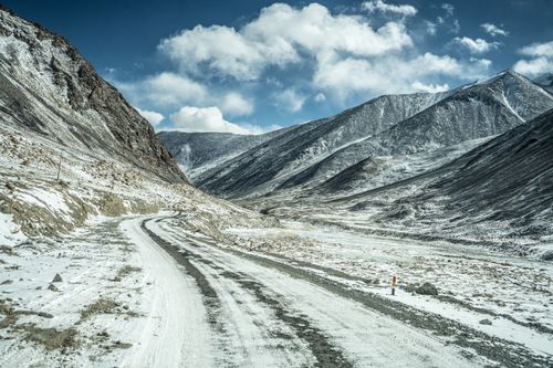Free Explore a winding dirt road through snow-covered mountains and valleys under a bright winter sky. Stock Photo