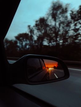 View of a stunning sunset reflecting in a car's side mirror while driving on a road.