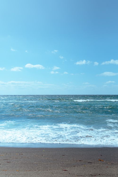Free Tranquil view of ocean waves and sandy beach under a bright blue sky. Stock Photo