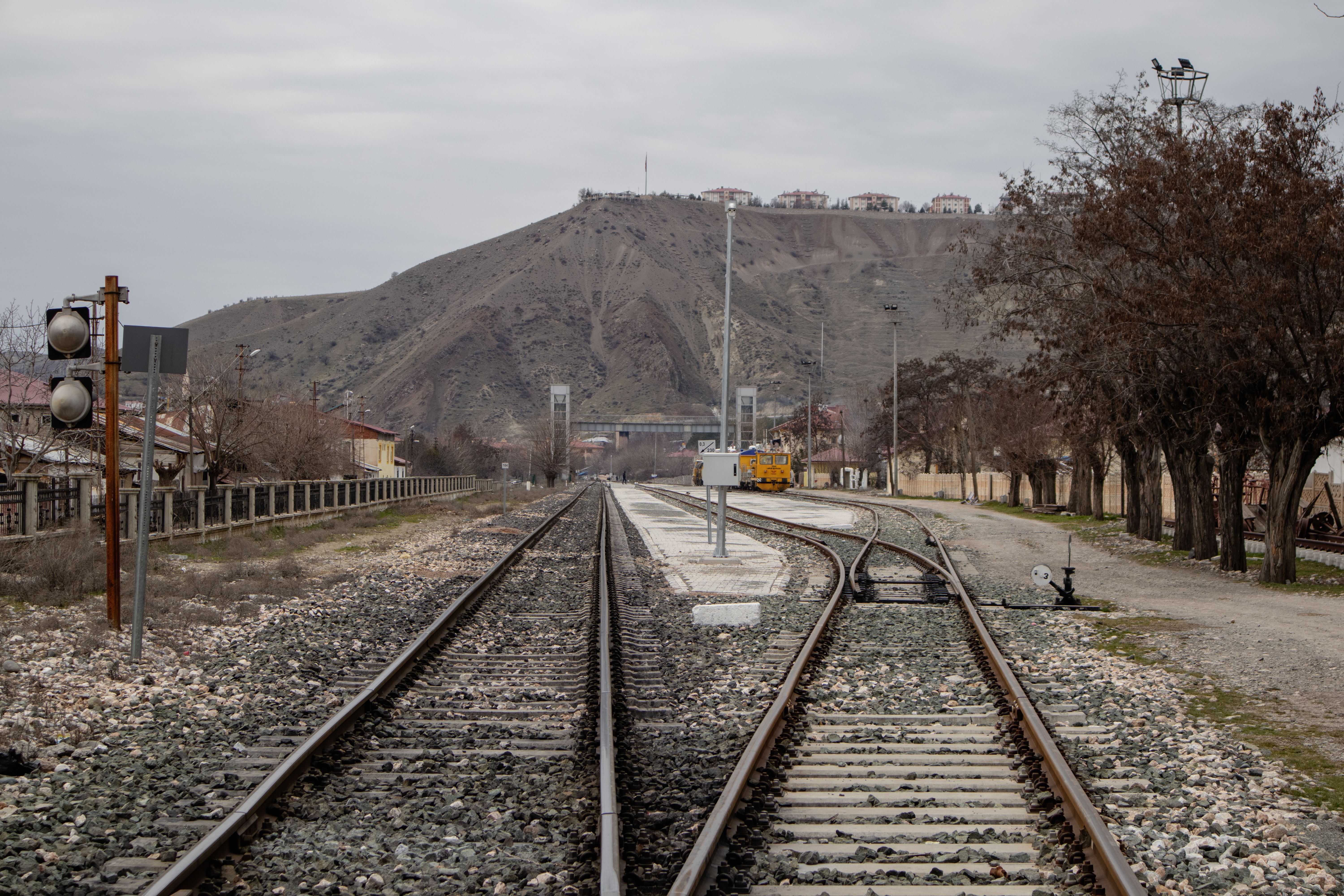 Railroad tracks leading through Palu, Elazığ, under a cloudy sky with scenic mountains in the background. (Photo by Zülfü Demir📸 on Pexels)
