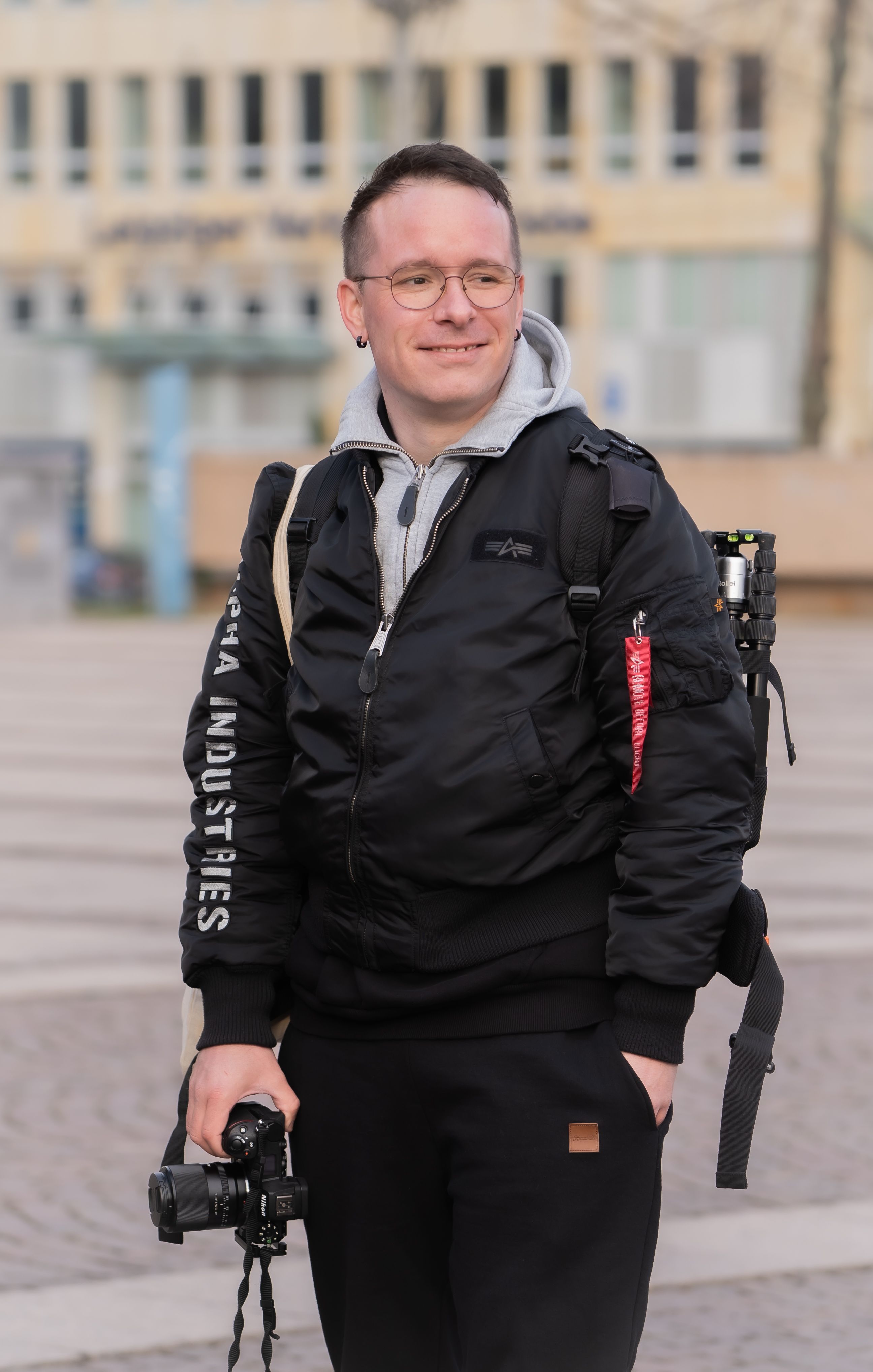 Portrait of a smiling photographer outdoors holding a camera, wearing a fashionable jacket.