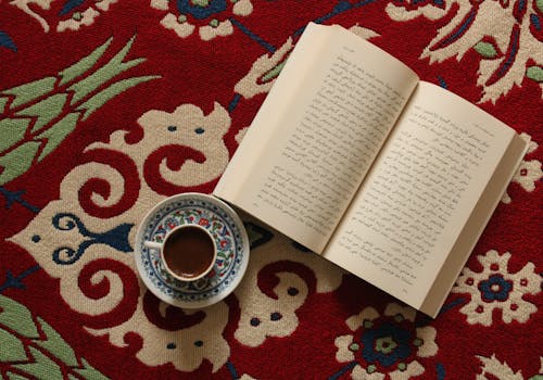 Top View of an Open Book and a Cup of Coffee on a Rug 