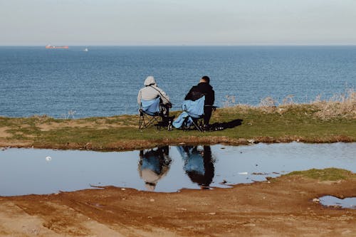 Two people sitting on a bench looking at the ocean