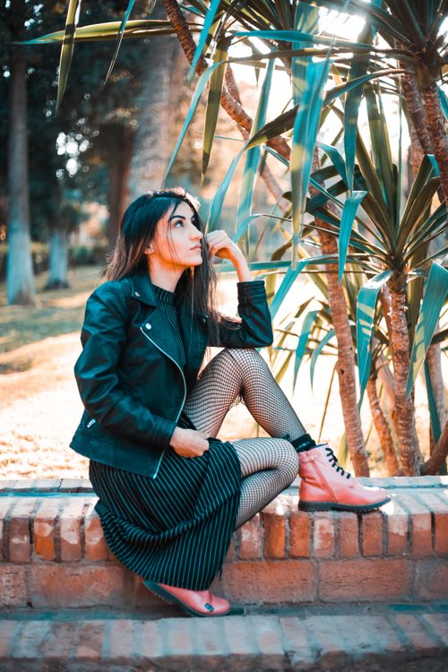 Free Fashionable woman in a black leather jacket posing in a park setting. Stock Photo