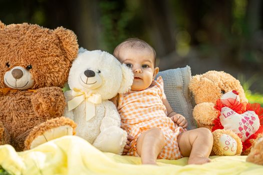 Cute baby sitting with teddy bears on a yellow blanket in a sunny park.