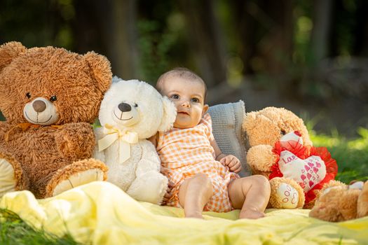 Cute baby in a summer picnic setting with teddy bears and a yellow blanket.