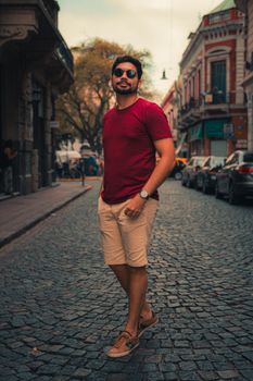 Trendy man in sunglasses walking on a cobbled city street in summer.