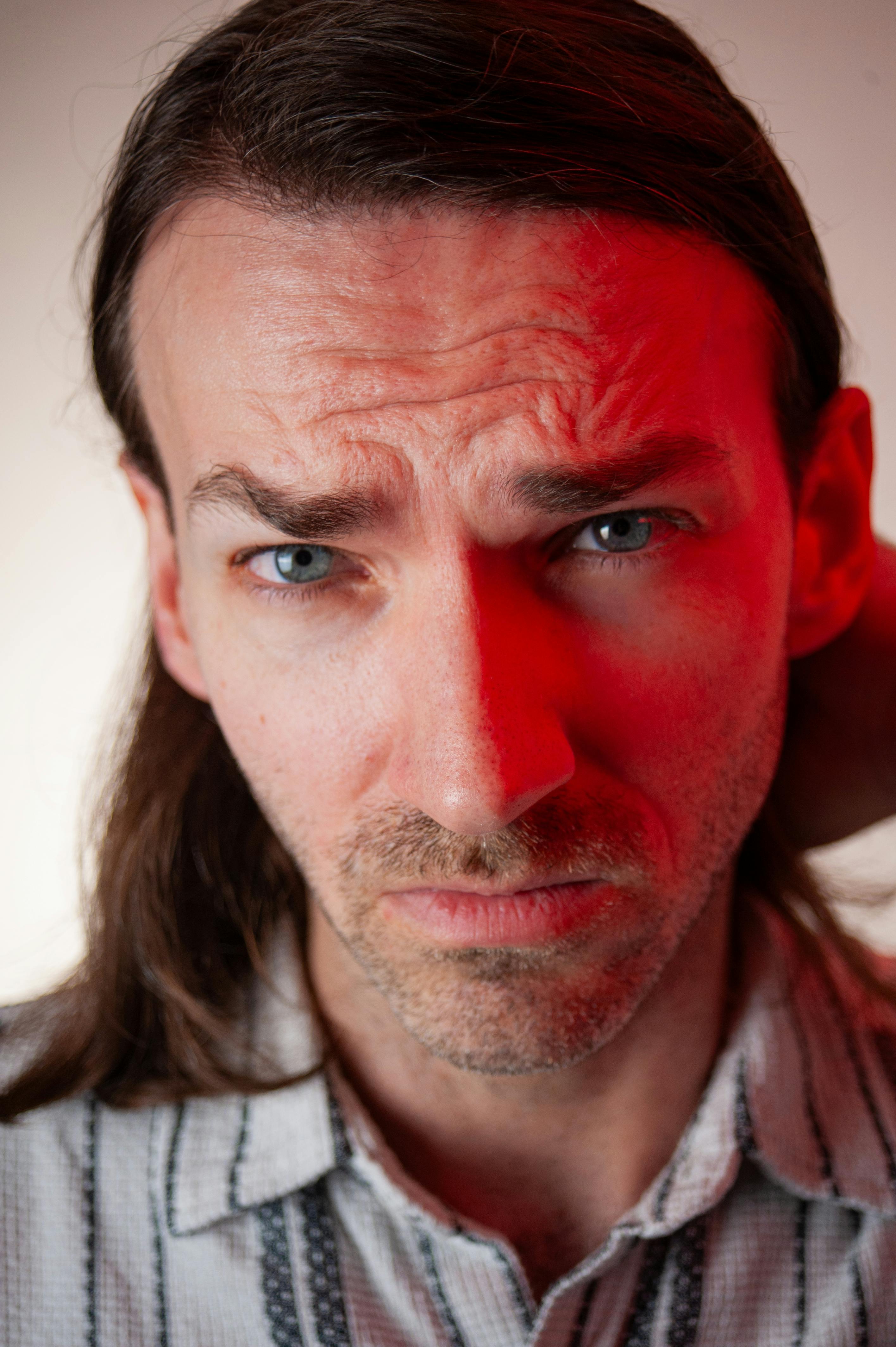 Close-up of a man with long hair and stubble, captured in dramatic lighting.