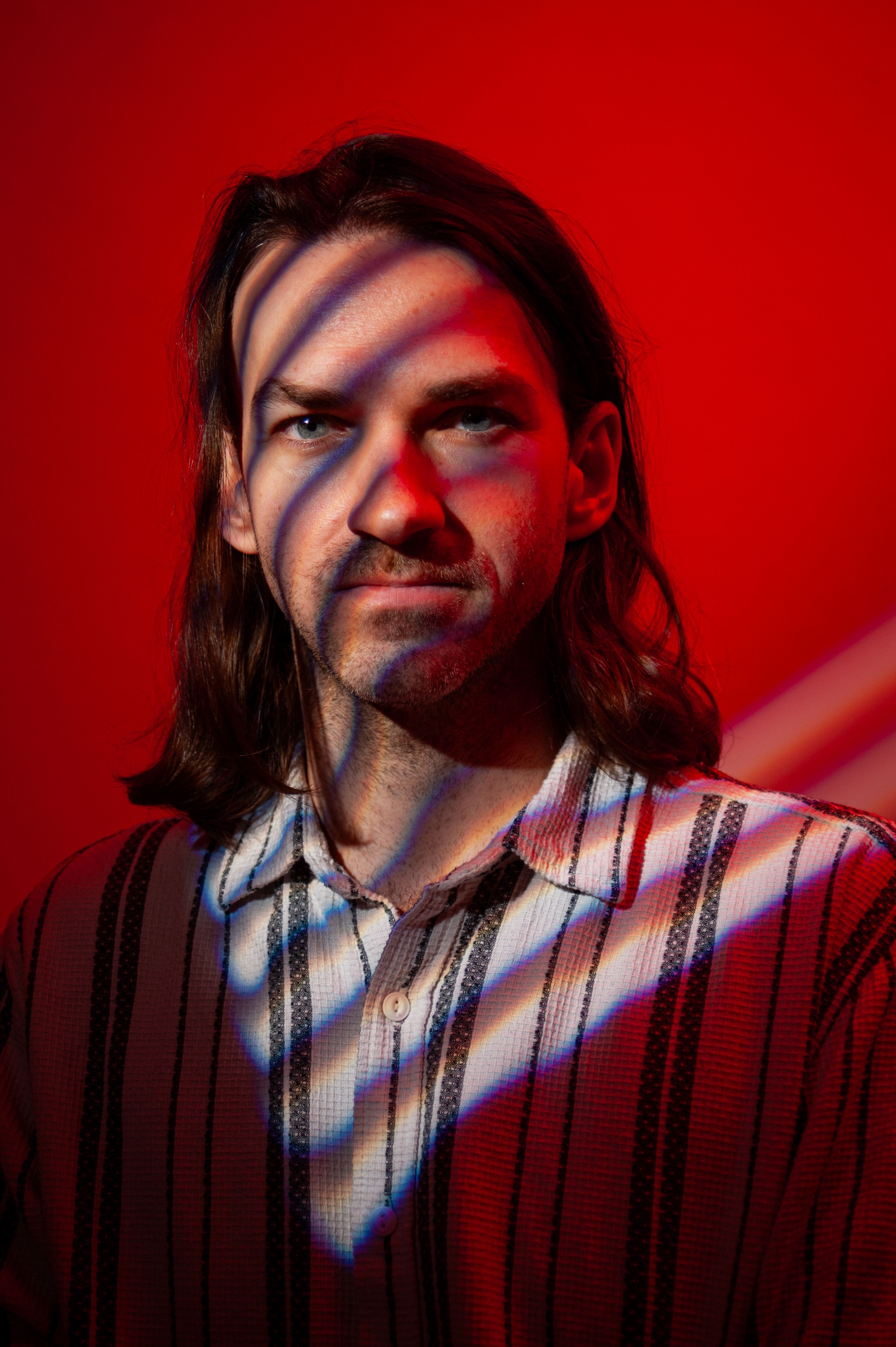 Portrait of a man with dramatic striped shadows on a vibrant red background.