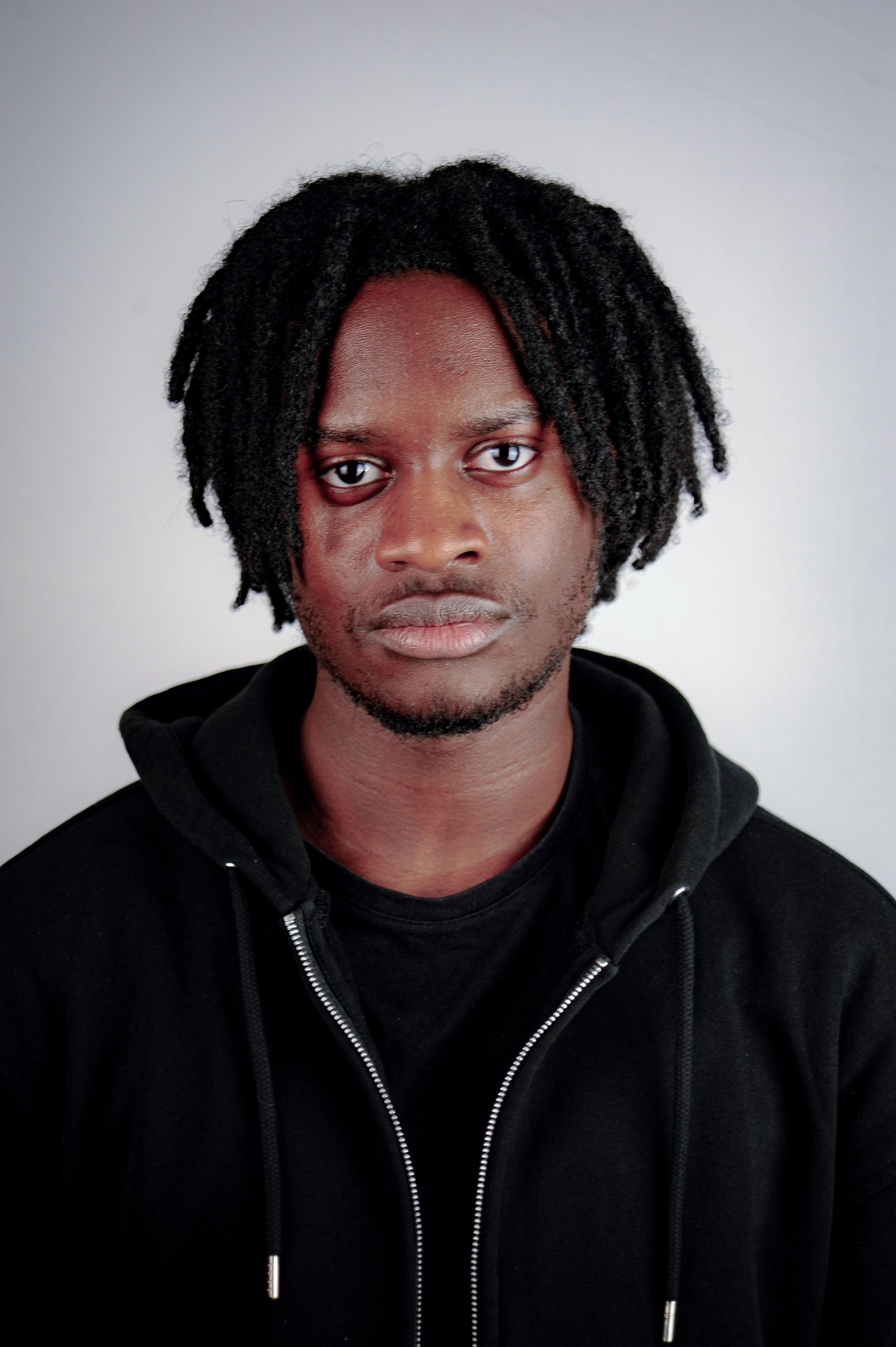 Studio portrait of a man with dreadlocks wearing a black hoodie against a white background.