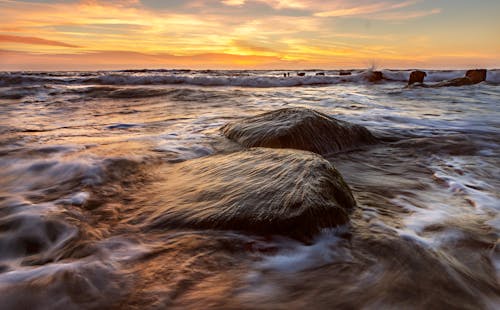 A sunset over the ocean with rocks in the water