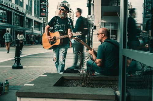 Free Two male musicians perform on a city street with guitars in a lively urban environment. Stock Photo